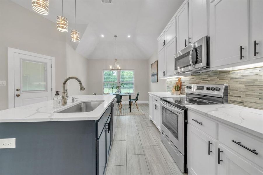 Kitchen with white cabinets, sink, appliances with stainless steel finishes, lofted ceiling, and a kitchen island with sink