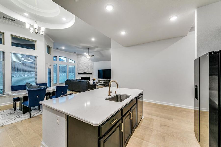 Kitchen with an island with sink, sink, light wood-type flooring, appliances with stainless steel finishes, and a fireplace