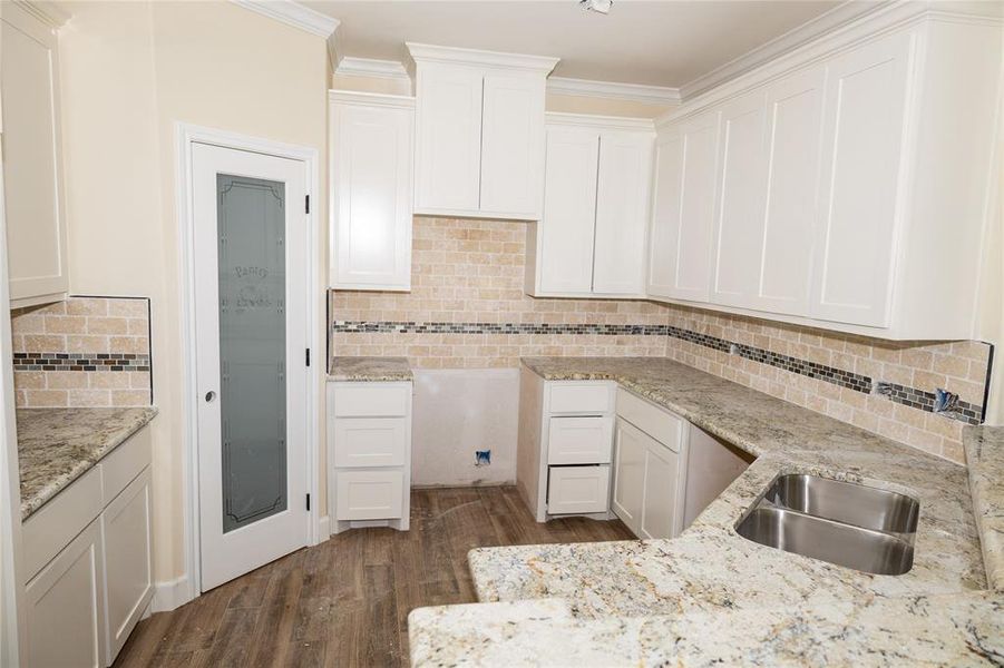 Kitchen with white cabinets, sink, light stone countertops, and dark wood-type flooring