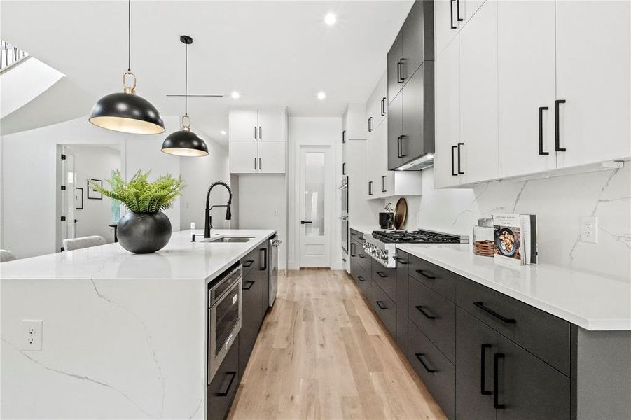 Kitchen with sink, light wood-type flooring, white cabinetry, pendant lighting, and a center island with sink