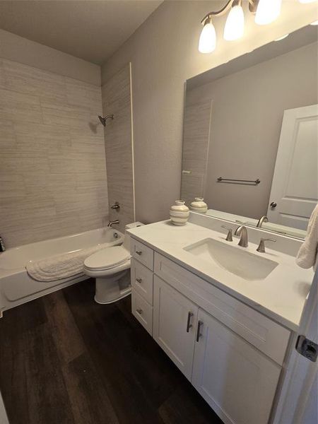 Full bathroom with wood-type flooring, vanity, tiled shower / bath combo, and toilet