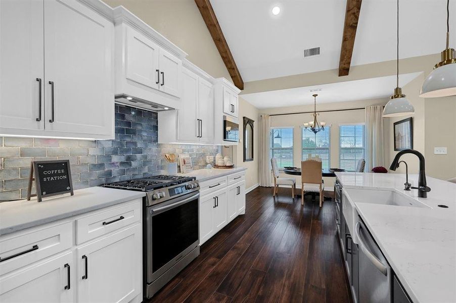 Kitchen featuring decorative backsplash, dark wood-type flooring, hanging light fixtures, stainless steel appliances, and white cabinets