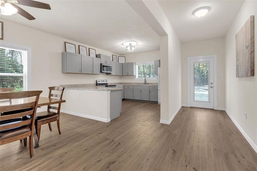 This is a bright and modern open-concept kitchen and dining area. The space features ample natural light, a ceiling fan, and direct access to the outdoors.