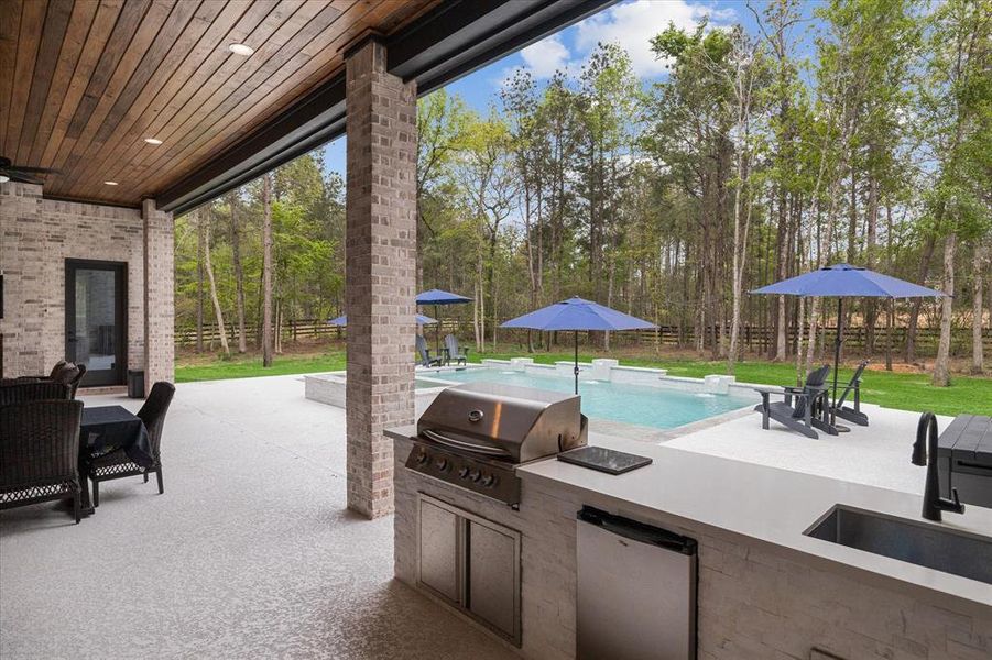 Outdoor kitchen with a grill, beverage refrigerator and large sink.