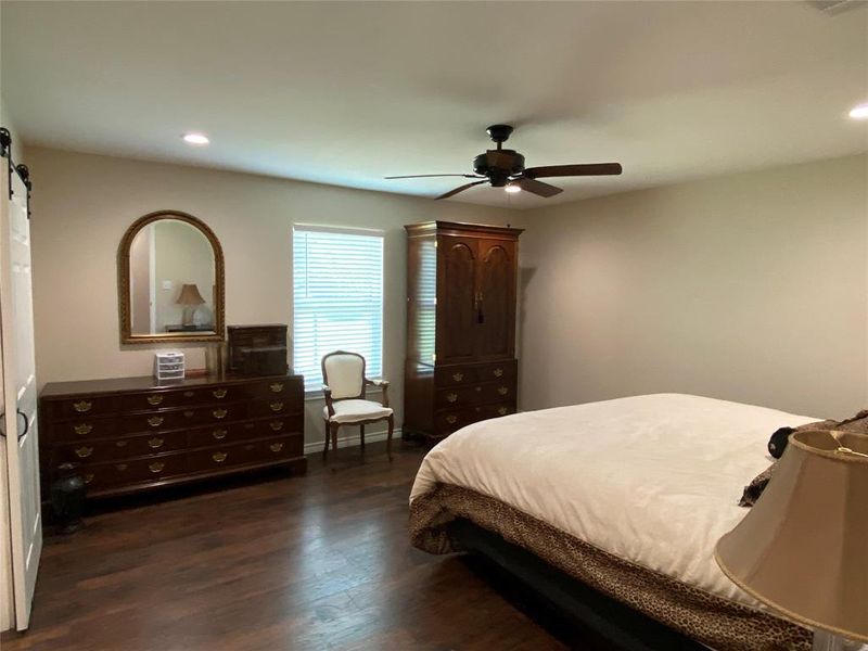 Bedroom with a barn door, ceiling fan, and dark hardwood / wood-style flooring
