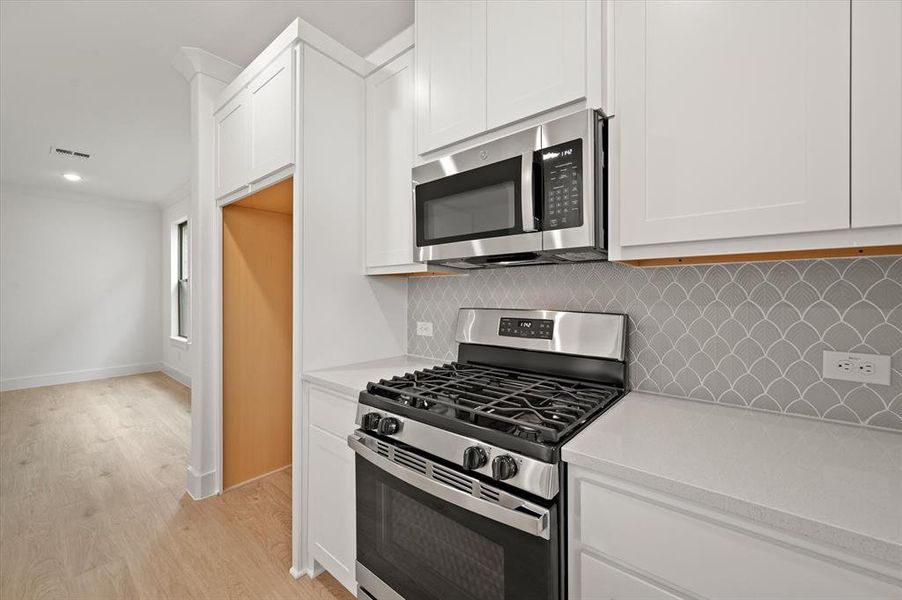 Kitchen with white cabinets, tasteful backsplash, light wood-type flooring, and stainless steel appliances