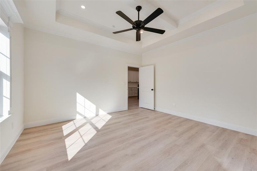 Empty room with a high ceiling, a tray ceiling, crown molding, light wood-type flooring, and ceiling fan