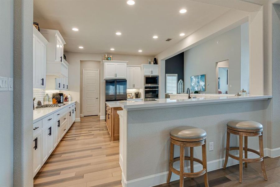 Kitchen with hardwood floors, kitchen peninsula, tasteful backsplash, stainless appliances and white cabinetry.