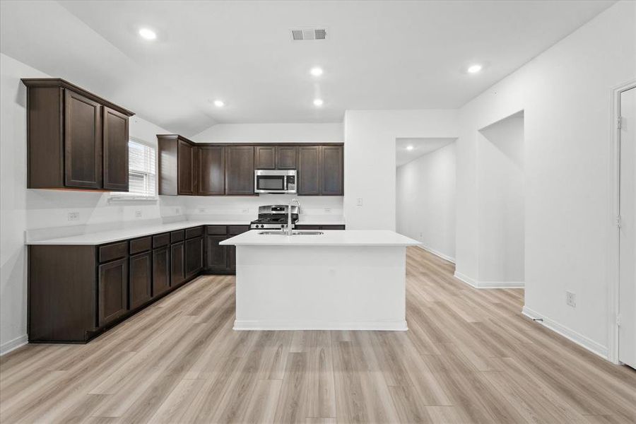 Kitchen with stainless steel appliances, light hardwood / wood-style flooring, a kitchen island with sink, and dark brown cabinetry