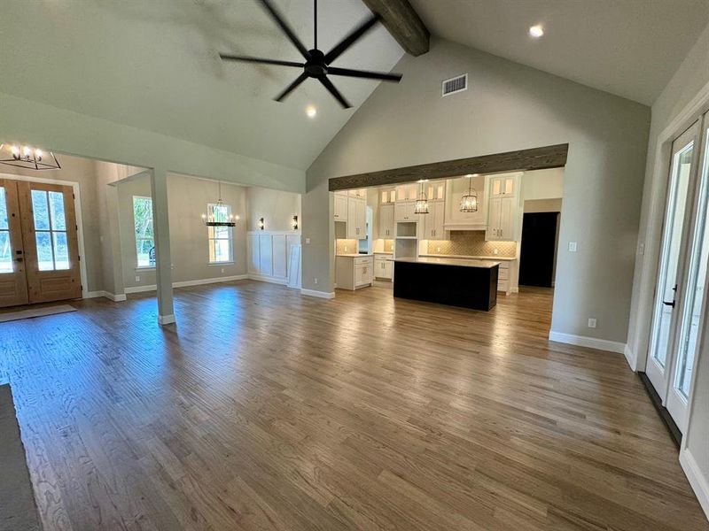 Unfurnished living room with wood-type flooring, beamed ceiling, french doors, and high vaulted ceiling