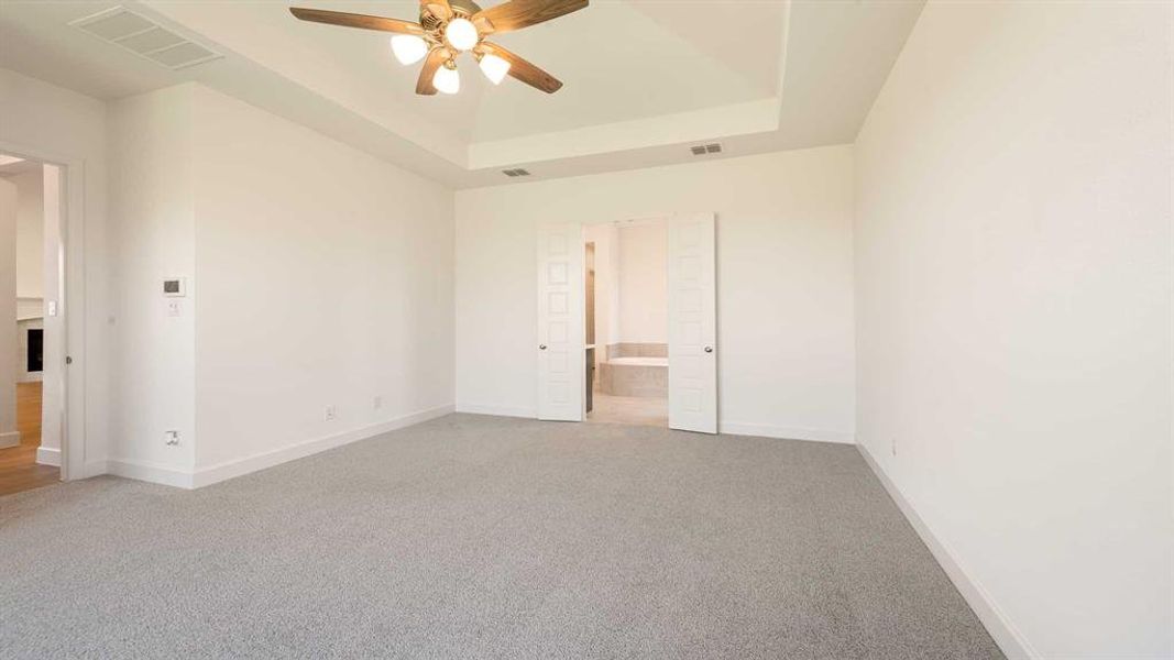 Unfurnished bedroom featuring ensuite bath, carpet flooring, a tray ceiling, and ceiling fan