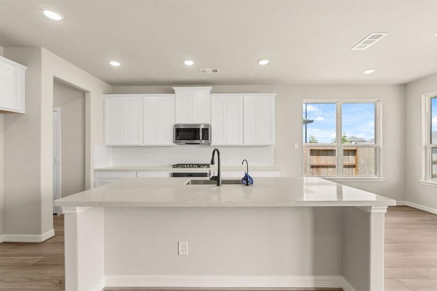 This light and bright kitchen features a large quartz island, white cabinets, a large sink overlooking your family room, recessed lighting, and beautiful backsplash.