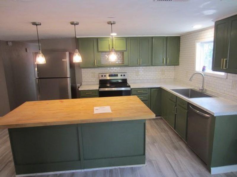 Kitchen with sink, stainless steel appliances, green cabinets, and butcher block counters