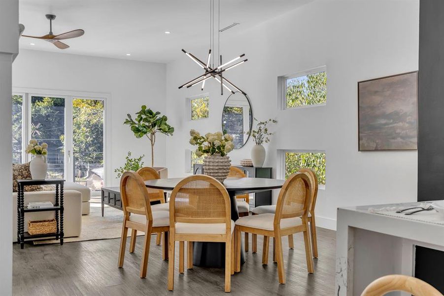 Dining space featuring a towering ceiling, hardwood / wood-style flooring, ceiling fan with notable chandelier, and plenty of natural light