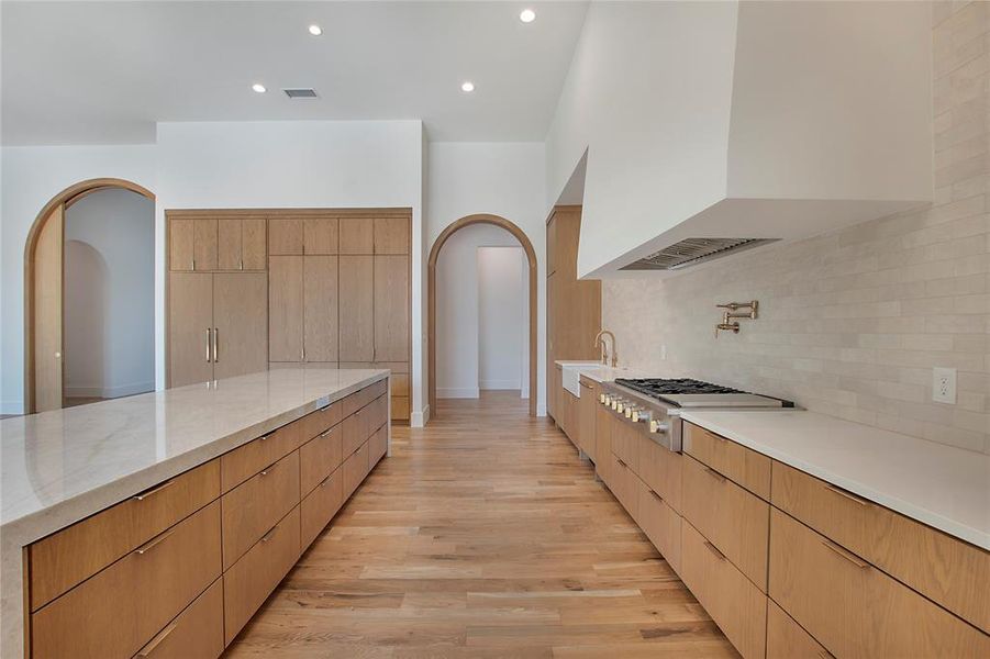 Kitchen featuring light hardwood / wood-style flooring, stainless steel gas stovetop, light stone countertops, backsplash, and premium range hood