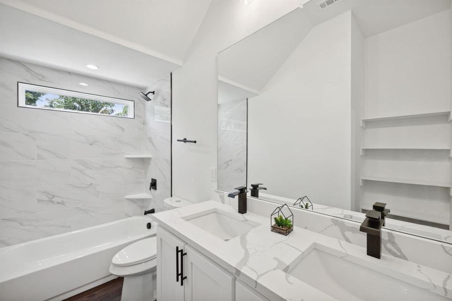 Full bathroom featuring dual bowl vanity, toilet, tiled shower / bath combo, and lofted ceiling