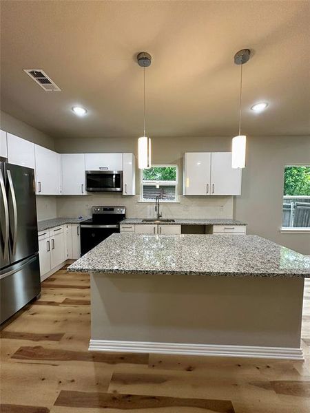 Kitchen with white cabinetry, stainless steel appliances, pendant lighting, light wood-type flooring, and a center island