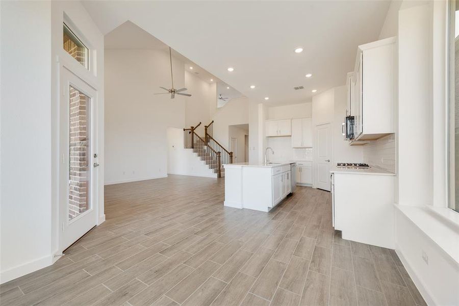 Kitchen with light hardwood / wood-style floors, white cabinets, sink, a kitchen island with sink, and high vaulted ceiling