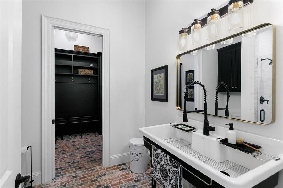 This stunning bathroom is off the mud room. Darling sink, gorgeous framed mirror, amazing light fixtures and a walk in shower. Notice the stunning brick floor. Mud room has more storage!  You will love all the storage this house offers!!!