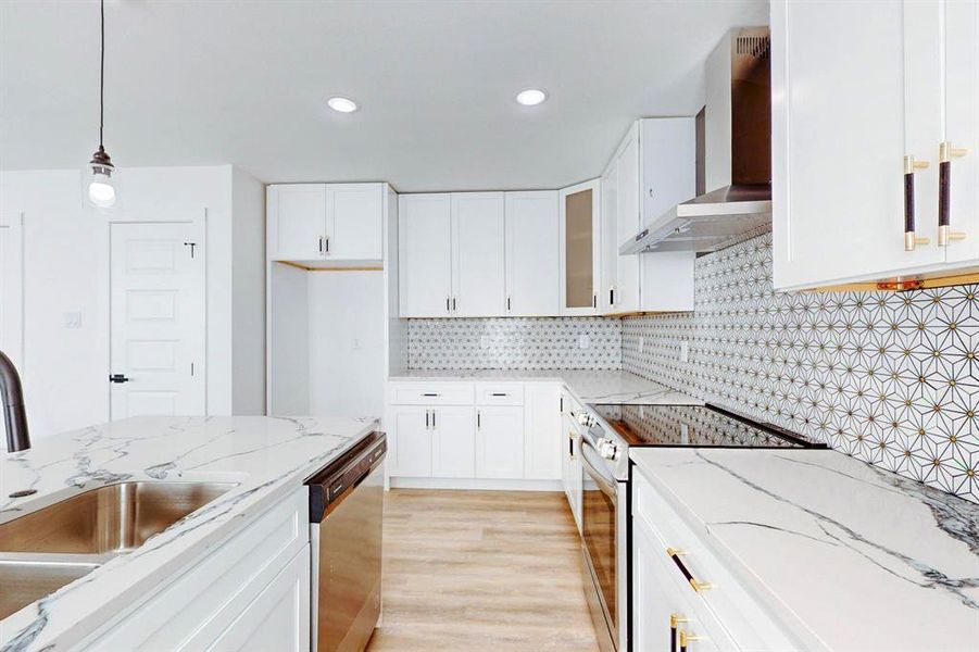 Kitchen with appliances with stainless steel finishes, hanging light fixtures, wall chimney range hood, and white cabinets