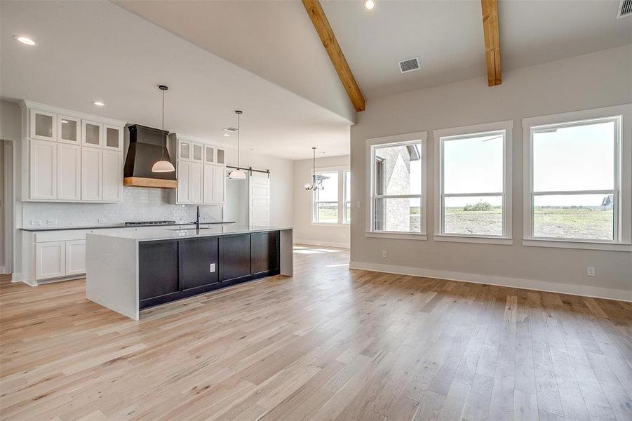 Kitchen with tasteful backsplash, decorative light fixtures, light hardwood / wood-style floors, custom exhaust hood, and an island with sink