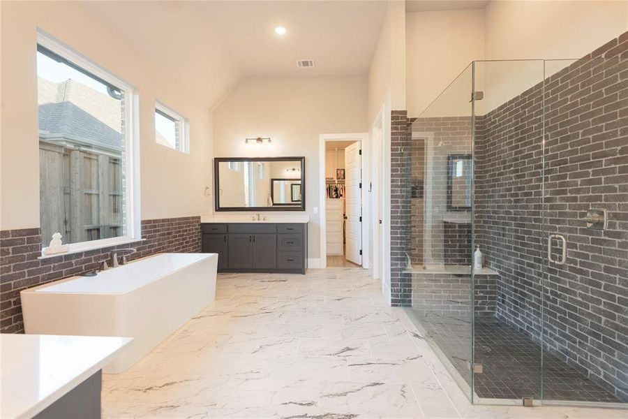 Bathroom featuring brick wall, vanity, plus walk in shower, and lofted ceiling