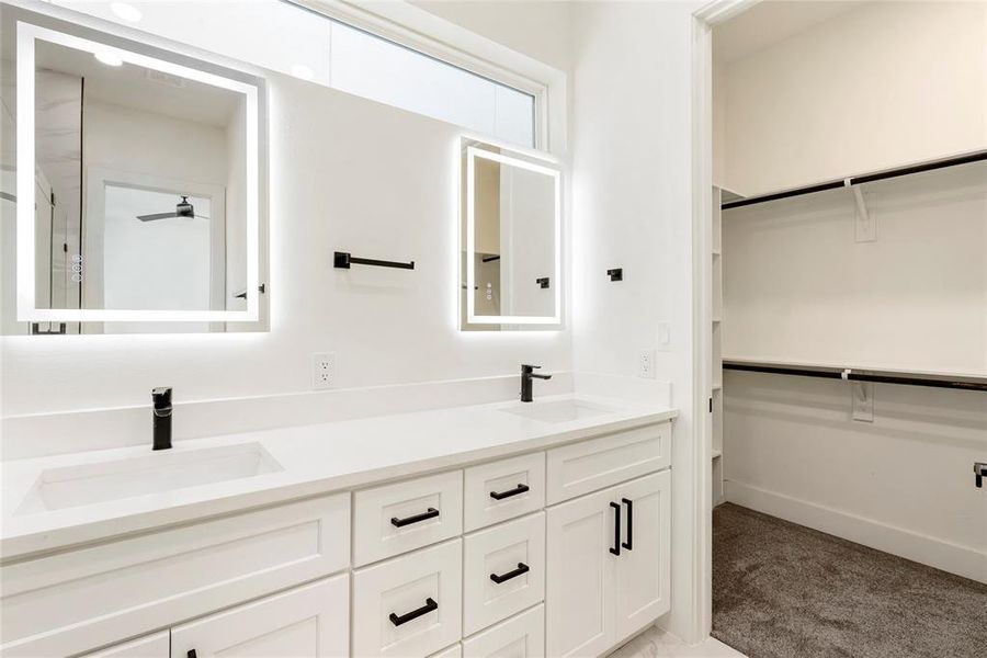 This photo showcases a modern bathroom with a double vanity and ample storage, including a walk-in closet with built-in shelving. The space features clean lines, backlit mirrors, and a neutral color palette.