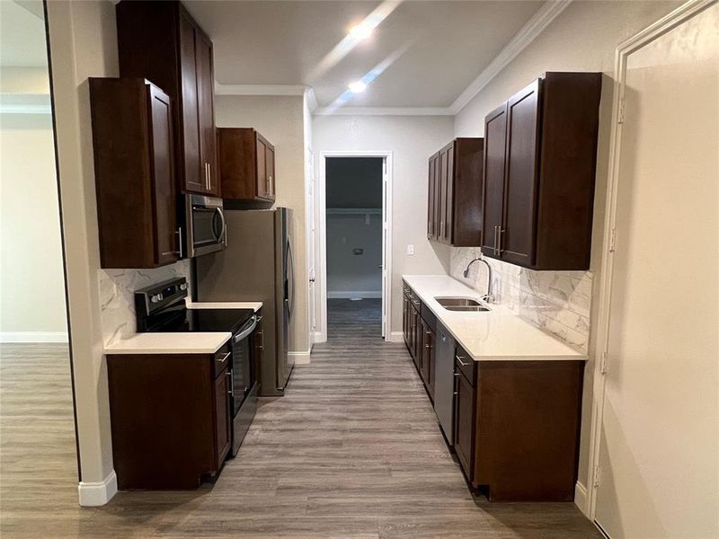 Kitchen featuring light wood-type flooring, appliances with stainless steel finishes, sink, and crown molding