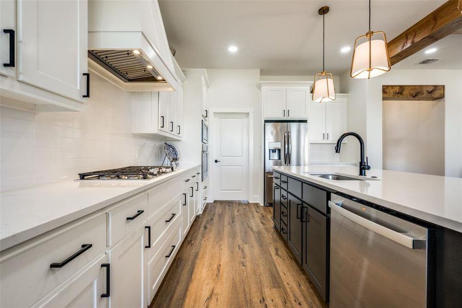 Kitchen featuring hardwood / wood-style floors, premium range hood, backsplash, white cabinetry, and appliances with stainless steel finishes