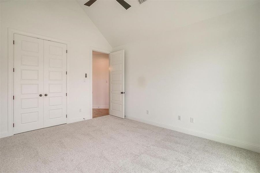 Unfurnished bedroom with high vaulted ceiling, ceiling fan, a closet, and carpet flooring