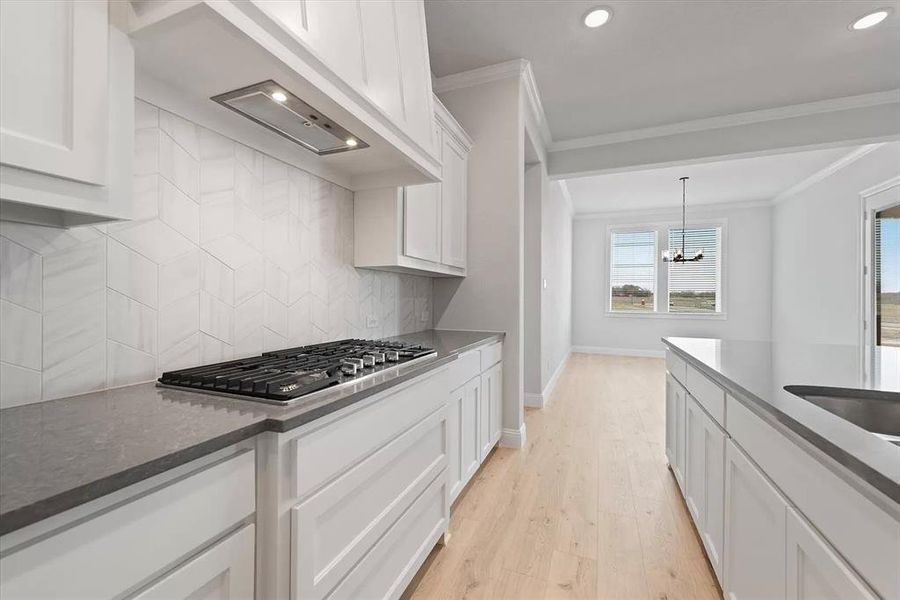 Kitchen featuring white cabinetry, light hardwood / wood-style flooring, stainless steel gas stovetop, decorative backsplash, and ornamental molding