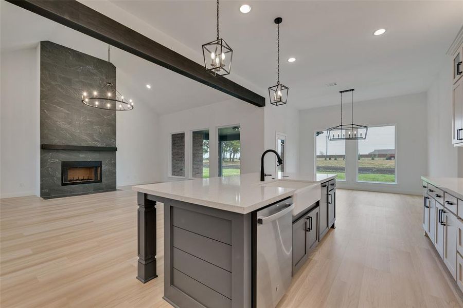 Kitchen featuring a premium fireplace, light hardwood / wood-style flooring, a notable chandelier, dishwasher, and an island with sink