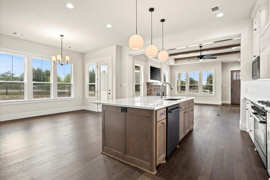 Kitchen with ceiling fan with notable chandelier, dark hardwood / wood-style flooring, a center island with sink, appliances with stainless steel finishes, and beam ceiling