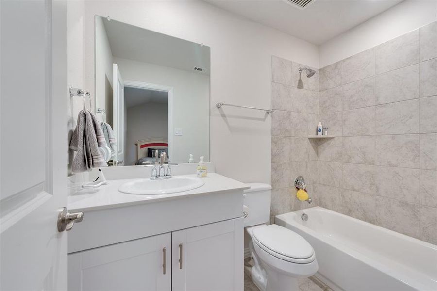 Full bathroom with vanity, tiled shower / bath combo, and toilet