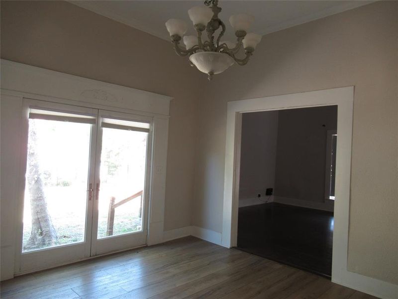 Empty room with crown molding, plenty of natural light, an inviting chandelier, and wood-type flooring