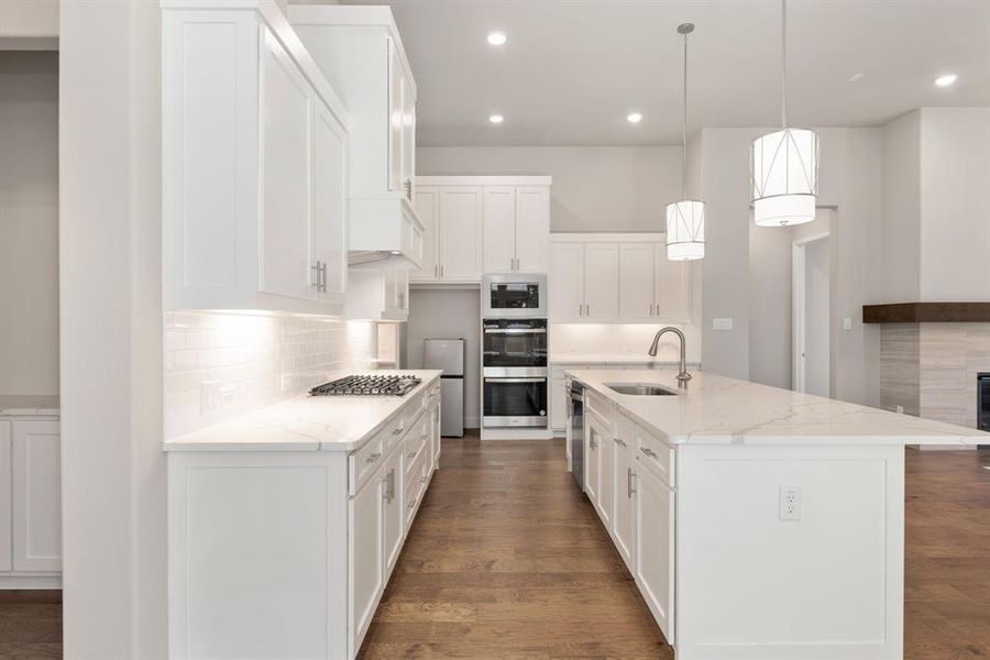 Kitchen featuring an island with sink, white cabinets, decorative light fixtures, and sink