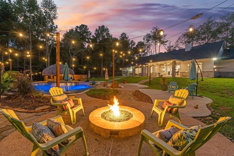 The firepit with its alluring glow draws your gaze, inviting you to gather around and enjoy cozy evenings with friends and family. Just to the right and behind the sparkling pool, you'll find four impressive 7-foot tall permanent gas tiki torches, casting a warm, enchanting light that dances in the night sky.