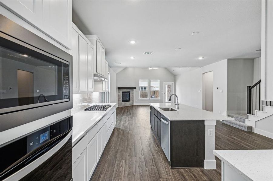 Kitchen featuring white cabinets, stainless steel appliances, sink, dark wood-type flooring, and a center island with sink