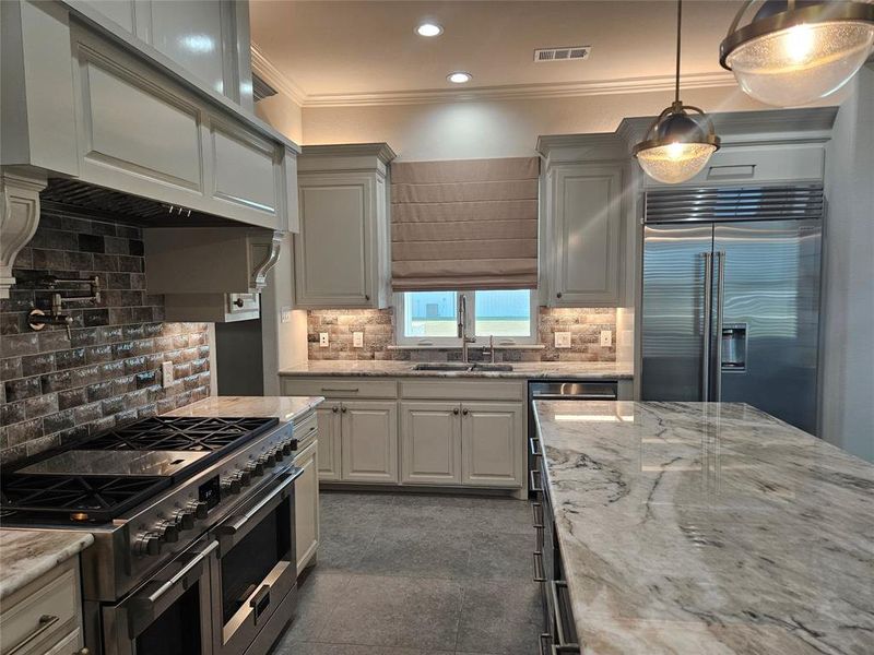 Kitchen featuring premium appliances, backsplash, hanging light fixtures, and ornamental molding