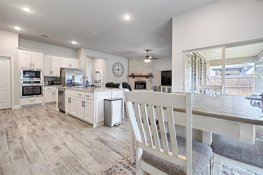 Kitchen with appliances with stainless steel finishes, a fireplace, white cabinetry, light hardwood / wood-style flooring, and a kitchen island with sink