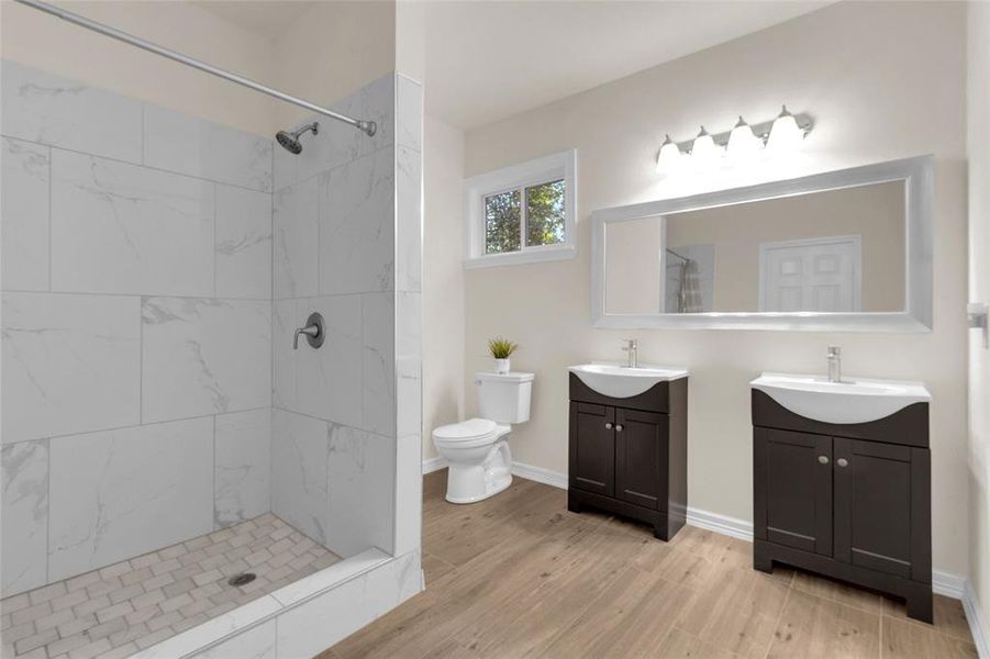 Modern bathroom featuring a walk-in shower with marble-like tiles, dual sinks with dark wood vanities, large mirror, and tile flooring. Bright space with natural light.