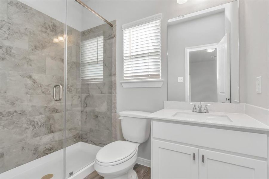 The en-suite bathroom features a sleek design with a glass-enclosed walk-in shower, modern tile work, and a spacious vanity. The large mirror and ample lighting create a bright, functional space that’s perfect for starting the day. This bathroom combines style and convenience, offering a private retreat for residents and guests alike. **This image is from another Saratoga Home with similar floor plan and finishes, not the June floorplan.**