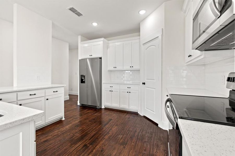 Kitchen featuring dark hardwood / wood-style floors, light stone countertops, appliances with stainless steel finishes, tasteful backsplash, and white cabinetry