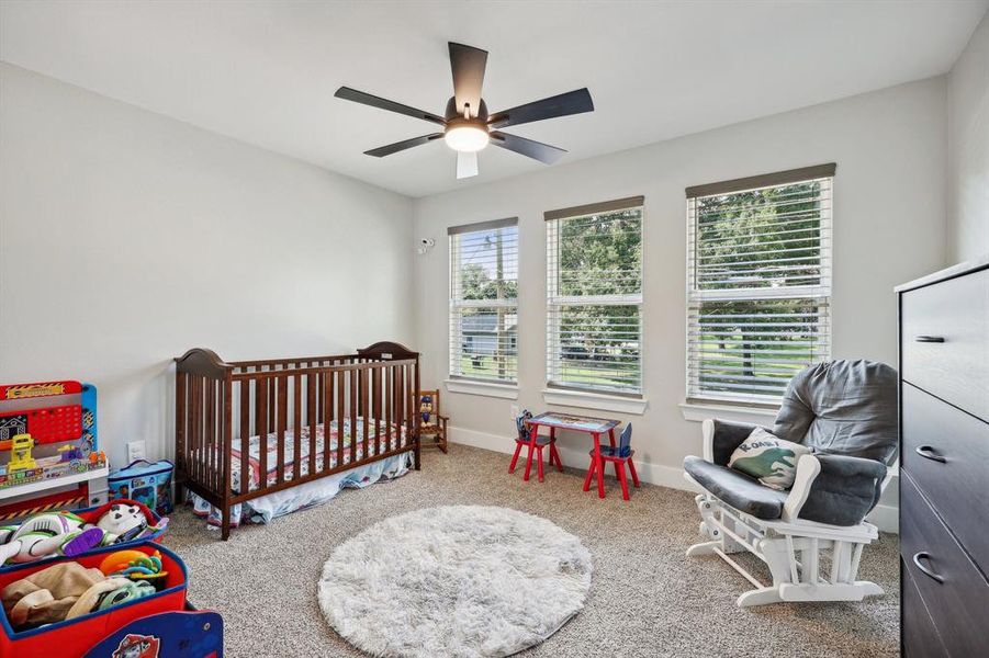 Carpeted bedroom featuring a nursery area and ceiling fan