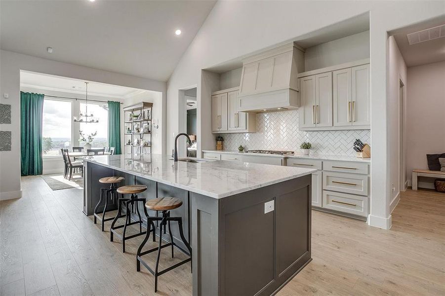 Kitchen with a large island with sink, sink, a kitchen breakfast bar, light hardwood / wood-style floors, and light stone counters