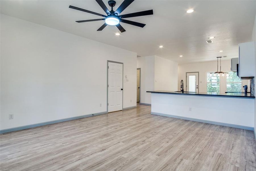 Unfurnished living room featuring ceiling fan with notable chandelier, light wood-type flooring, and sink