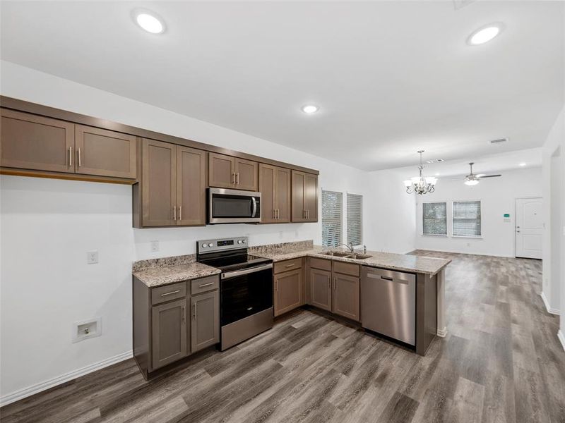 Kitchen featuring kitchen peninsula, wood-type flooring, sink, pendant lighting, and appliances with stainless steel finishes