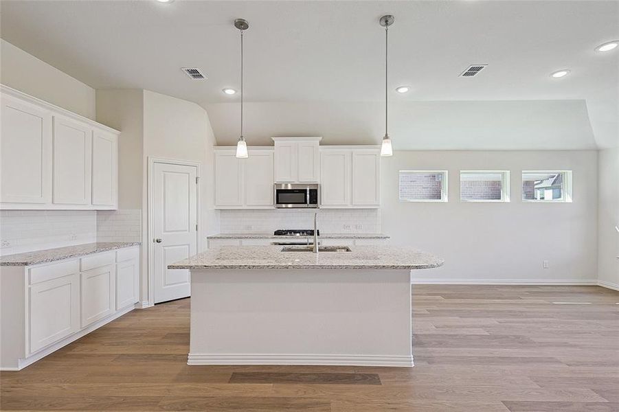 Kitchen featuring white cabinetry, light hardwood / wood-style floors, decorative light fixtures, and light stone counters