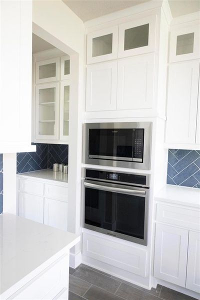 Kitchen featuring white cabinets, backsplash, light stone countertops, and stainless steel appliances