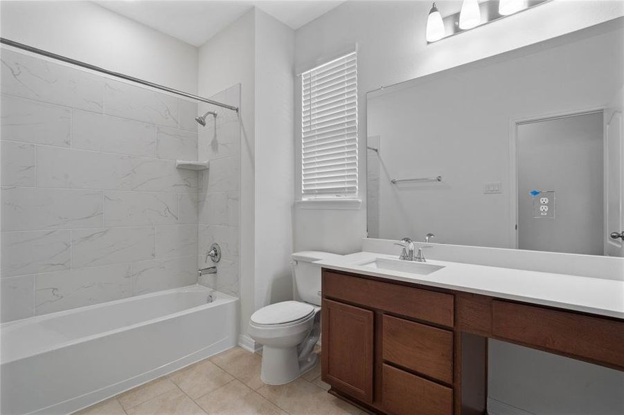 Secondary bathroom features light countertops and stained cabinets, neutral paint, shower/tub combo with tile surround, large mirror, tile floors, sleek fixtures and modern finishes, plenty of space to accommodate any visiting family or guests.